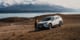 White GO Rentals SUV parked on a dry landscape with mountains and a lake in the background